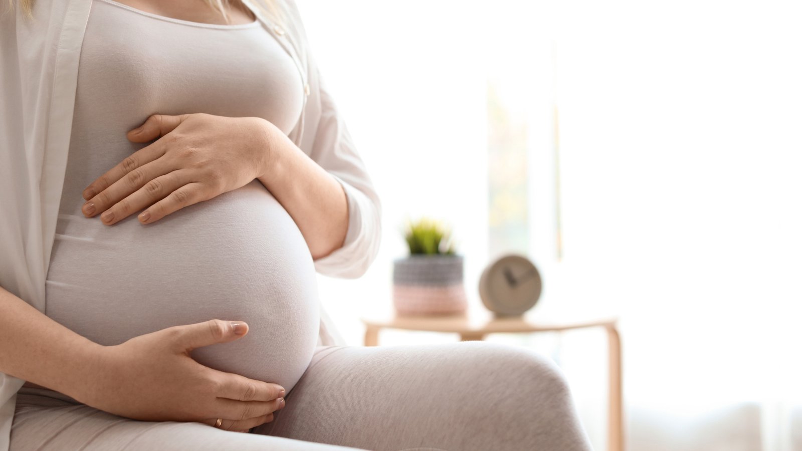 Mulher grávida segurando a barriga em casa, representando os resultados de tratamentos de fertilidade e fatores que influenciam a taxa de sucesso da IVM.
